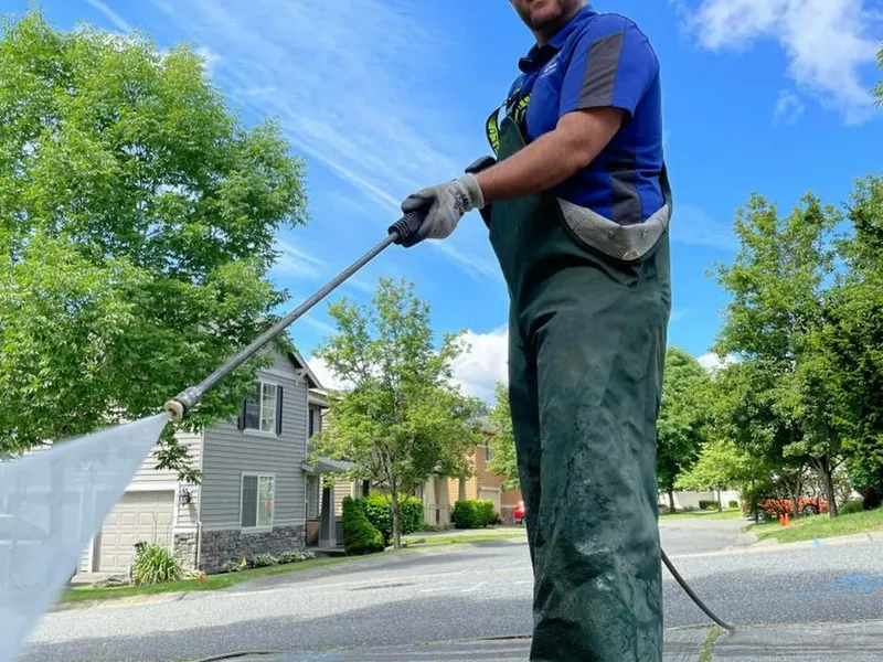 A technician power washing a residential driveway, water spray catching the bright Arizona sunlight