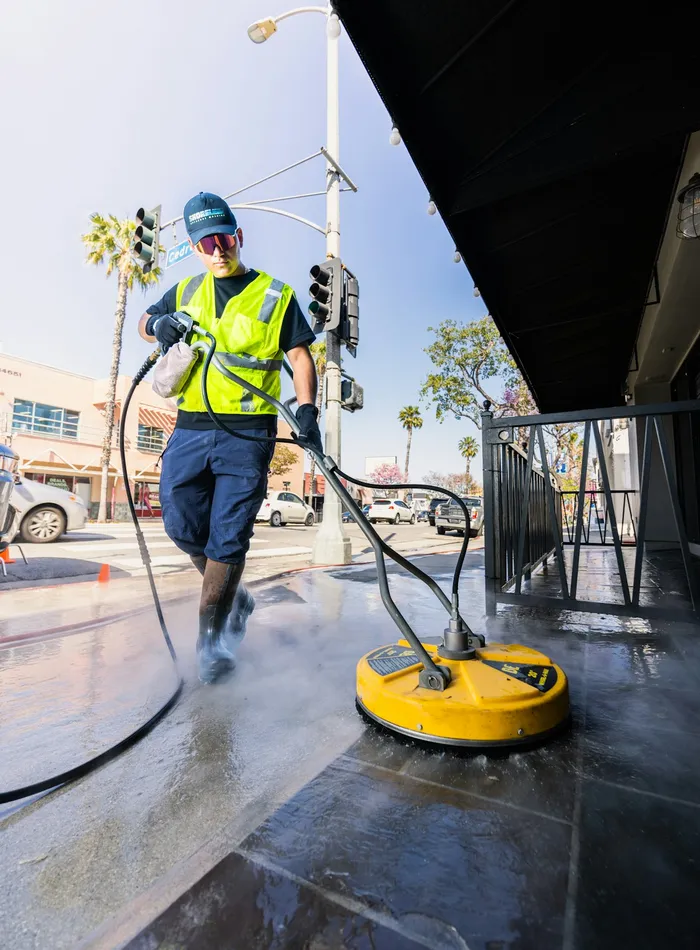A Sunridge Pressure Washing technician operating a surface cleaner on a sunny sidewalk
